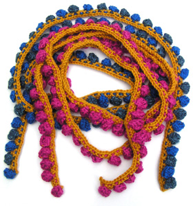 Rätstickade gula smala halsdukar tätt instickade moucher i rosa eller blått.