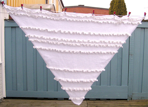 Slätstickad vit trekantsjal med vita glansiga volanger.